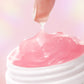 Pink cream being squeezed out of a white container on a pink background