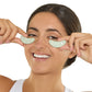 Woman applying green eye patches to her eyes on a white background