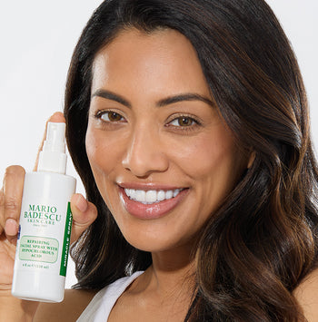 Woman holding a Mario Badescu skincare product against a white background